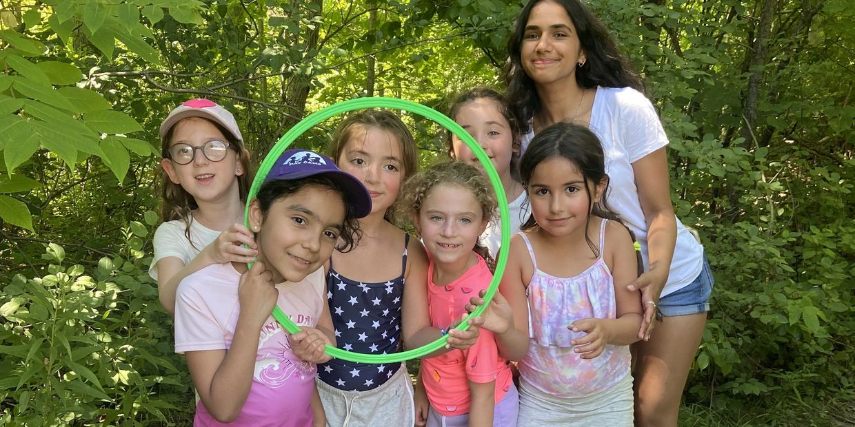 a group of girls in nature smiling while posing with a green hula hoop 