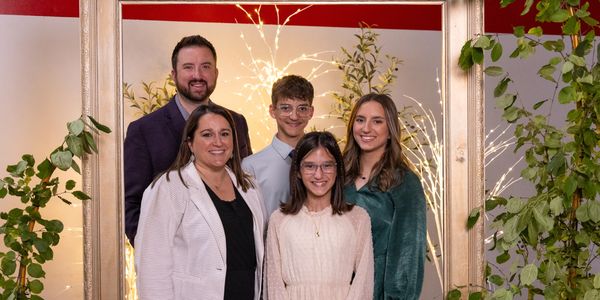 A happy family of five posing together indoors with a decorative frame and lights.