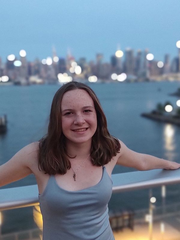 Young woman smiling on a balcony with city lights over water in the background.