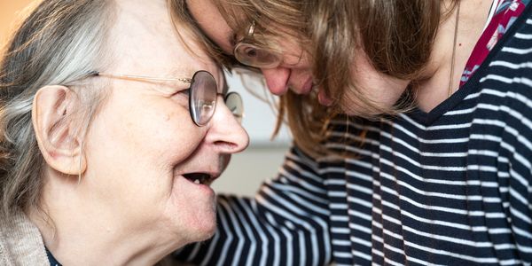 An older woman and younger woman touch their foreheads together in a gesture of intimacy smiling