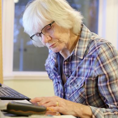 An older woman sitting at her computer looking at papers