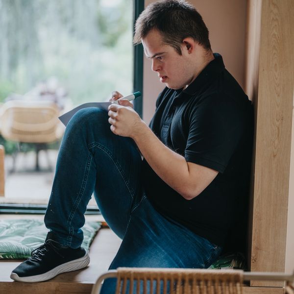 A young man sitting on the floor writing in a journal