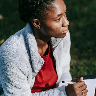A young woman sitting outside with a notebook and pen, gazing into space thinking