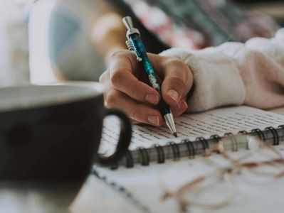 A close up of a hand holding a pen, writing in a journal