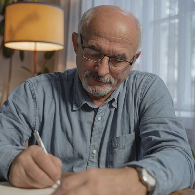 An older man sitting indoors, writing in a journal.