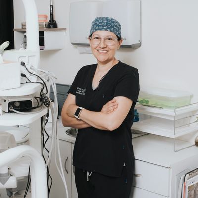 Female dentist in scrubs smiling confidently in a dental clinic.