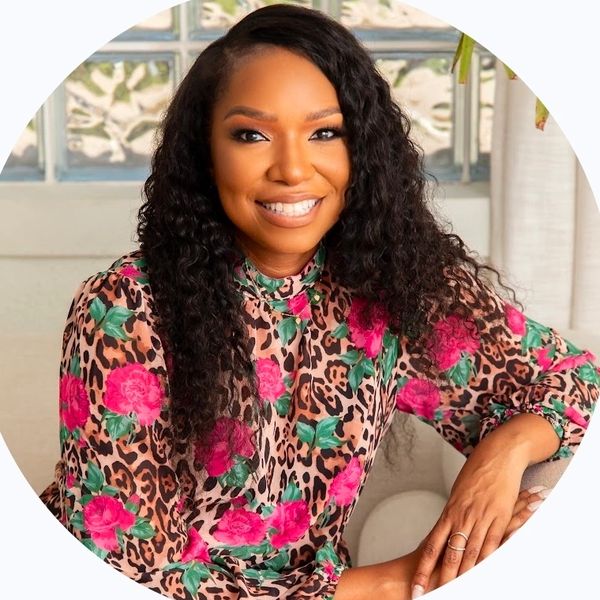 Smiling woman with curly hair in a floral and leopard print blouse.