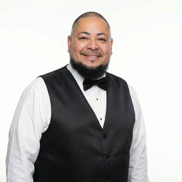 Smiling man wearing a black vest and bow tie over a white shirt.