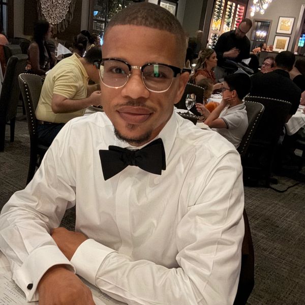 Man in white shirt and black bow tie sitting at a restaurant table.