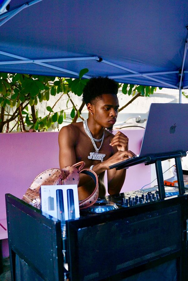 Young shirtless DJ focused on mixing music under a blue canopy.