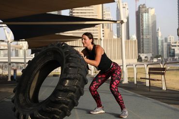 A woman flips a large tire during an outdoor workout in an urban setting.
