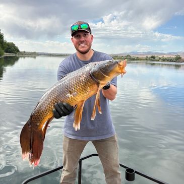 Man holding a large fish by a lake.