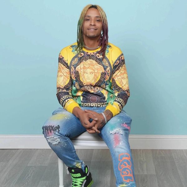 Man with colorful dreadlocks sitting on a chair against a blue wall.