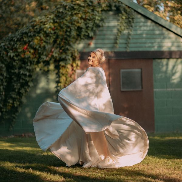 Bride twirling in ivory satin cape wedding dress made by Susie Grist Couture