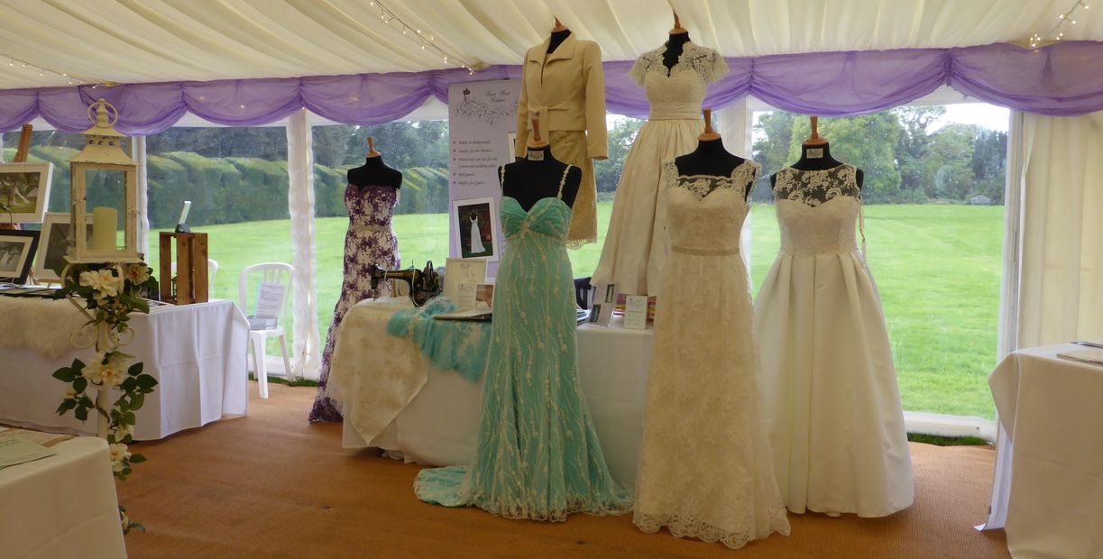 Six wedding dresses by Susie Grist Couture on and around a table at a wedding fair in a marquee