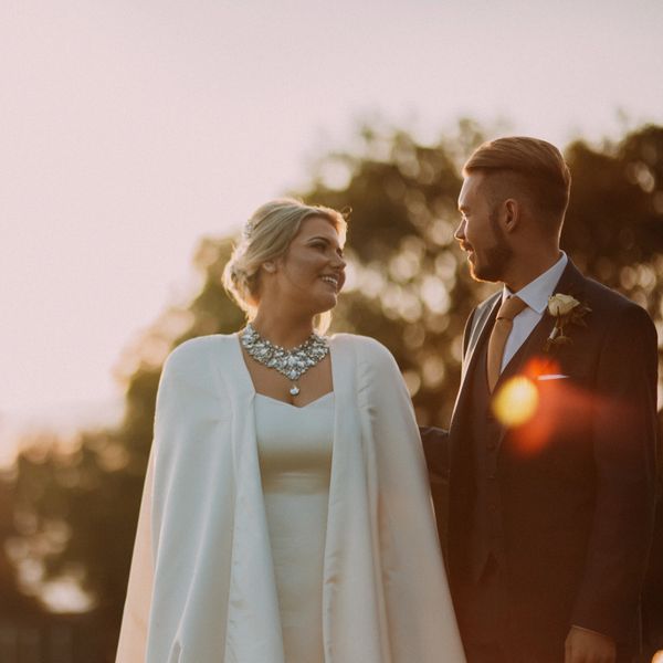 Bride and groom at sunset looking at each other. bride is wearing ivory satin cape wedding dress