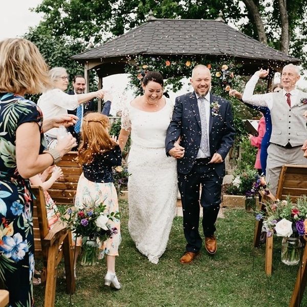 Bride and groom walking down the aisle of an outside ceremony being showered with confetti