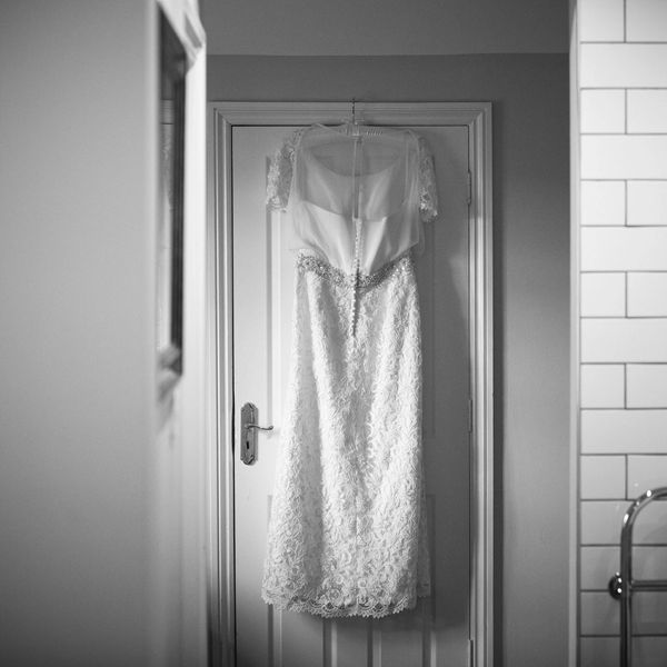 A wedding dress hanging on a door made from ivory chiffon, crepe and beaded guipure lace