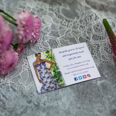 Business card of Susie Grist Couture layed on a lace background surrounded by pink flowers
