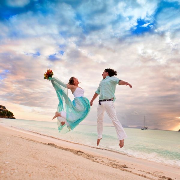 Bride and groom jumping in the air by the sea. Wedding dress has white lace top, aqua chiffon skirt