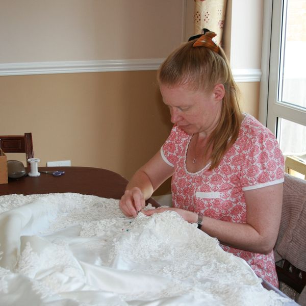 Susie hand sewing lace trim to the hem of a wedding dress