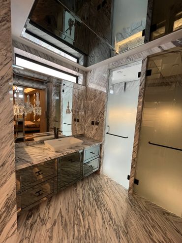 Luxurious bathroom with marble walls, mirrored cabinets, and frosted glass doors.