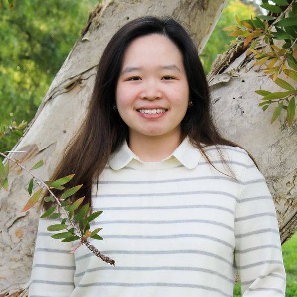 Hilary Ghozali, smiling in casual attire outdoors by a tree