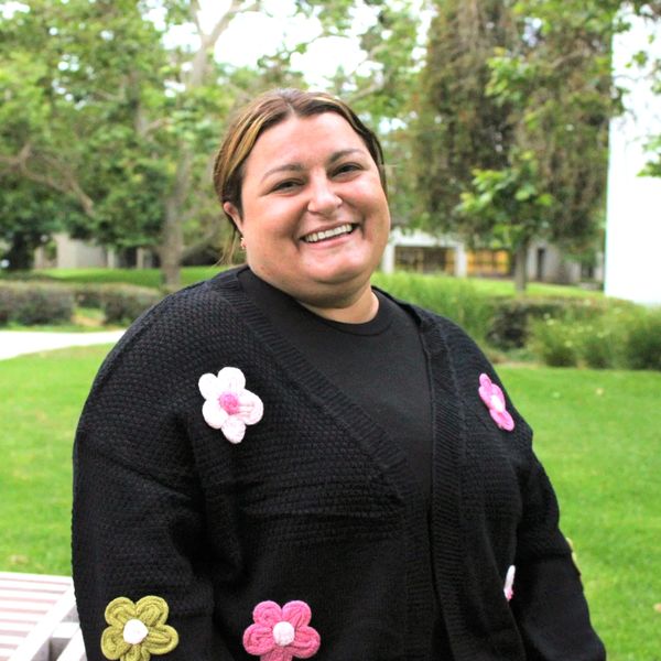 Smiling woman in a black sweater with colorful flower patches outdoors.