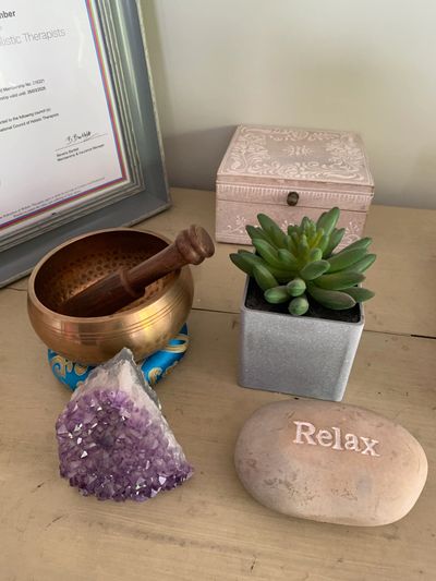 A relaxing setup with a singing bowl, amethyst crystal, succulent plant, and a stone inscribed with 'Relax'.