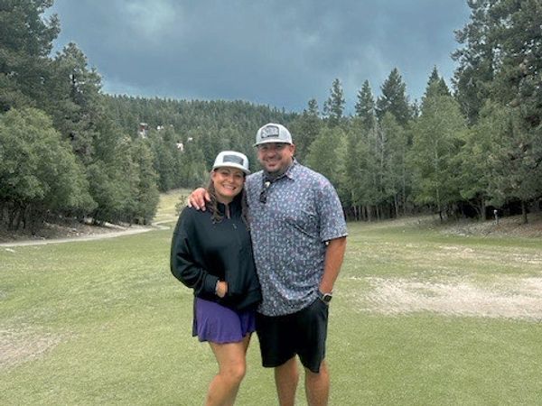 A couple posing on a golf course under a cloudy sky.