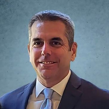 A man in a suit and tie smiling against a blue textured background.