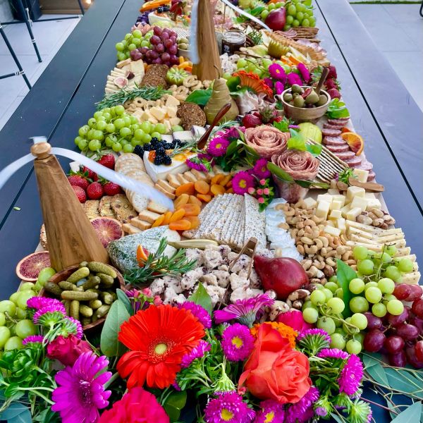 A colorful charcuterie board with fruits, cheeses, nuts, and flowers.