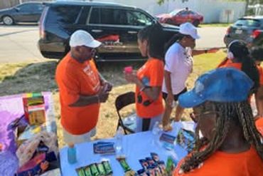 People in orange shirts setting up a snack table outdoors.