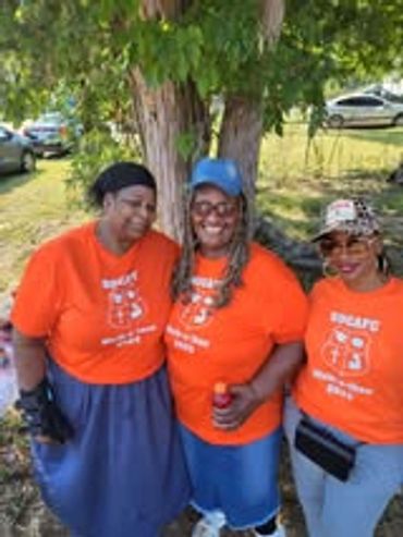 Three women wearing matching orange shirts and smiling outdoors.