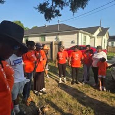 Group of people wearing orange shirts gathered outdoors near houses.