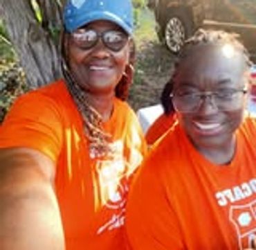 Two smiling women wearing matching orange shirts outdoors.