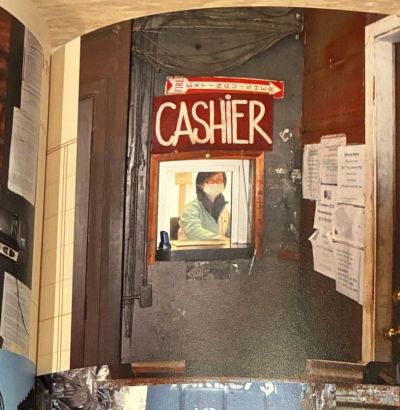 Cashier behind a small window in a rustic setting.
