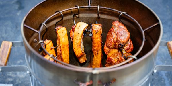 Meat and vegetables roasting inside a vertical smoker with hooks.
