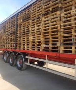 A truck loaded with wooden pallets stacked high.