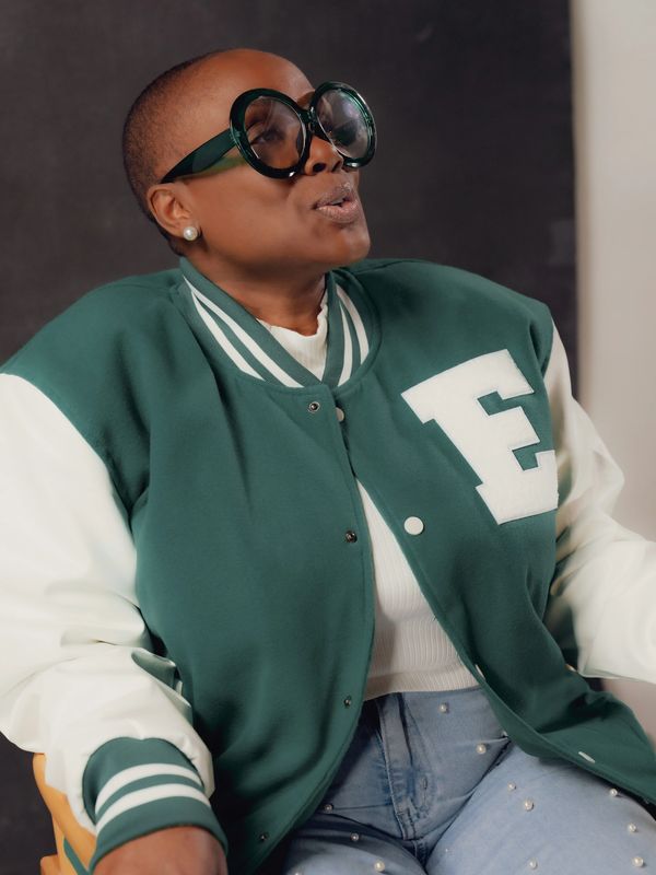 Person wearing oversized glasses and green varsity jacket.