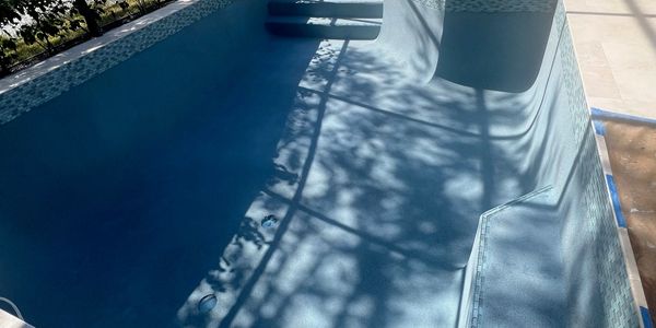 Empty pool with shadows of a fence and trees.