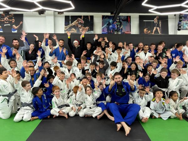 Large group of martial arts students and instructors posing and waving, dressed in gis.