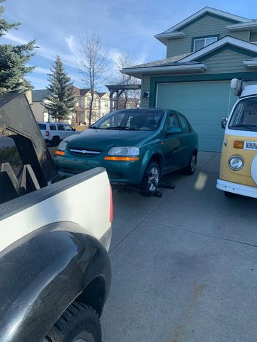 A green car being towed in a residential driveway on a clear day.