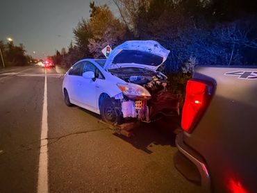 A white car with front damage is being towed at night on a road.
