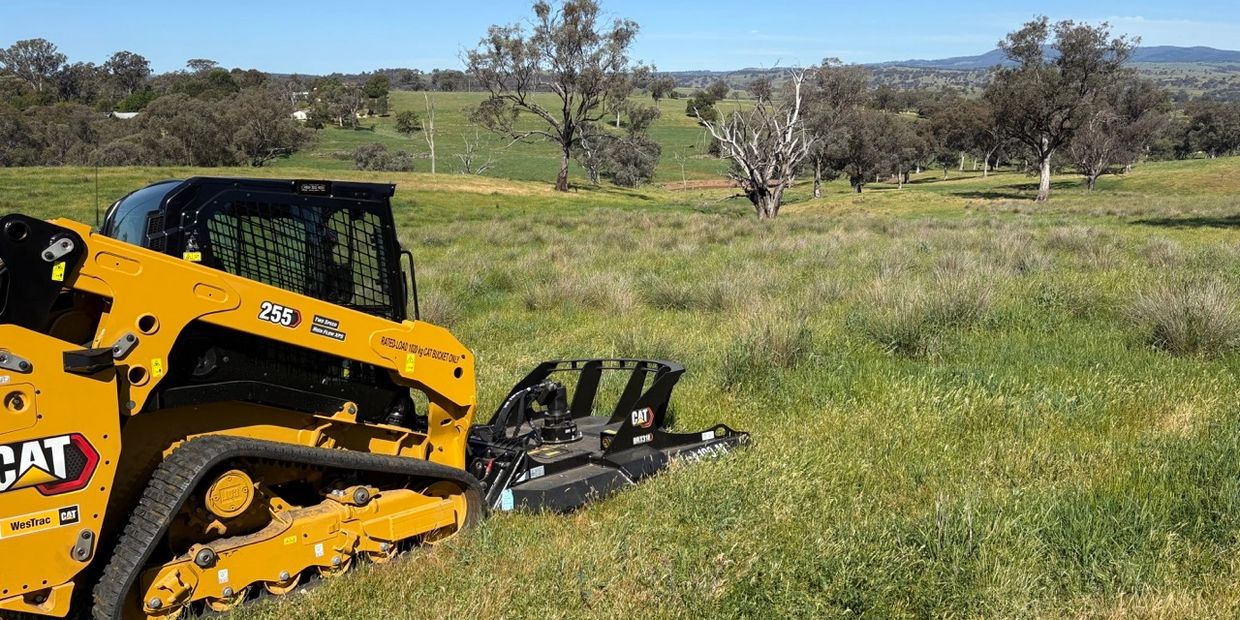 Yellow CAT 255 tracked loader mowing grass in a green field under a blue sky.