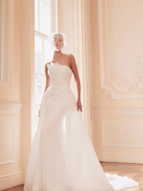 Model in a white strapless wedding gown with a veil in a softly lit room.