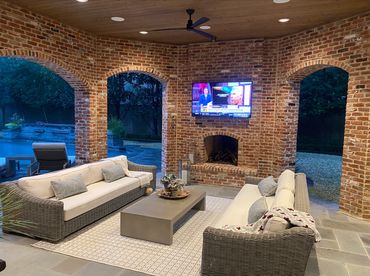 Cozy outdoor patio with brick walls, wicker sofas, and a TV above a fireplace at night enjoying premium ceiling speakers and exceptional WiFi