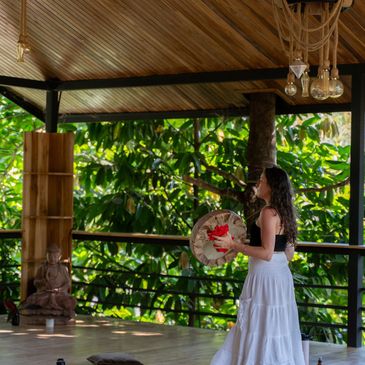 Woman in white skirt holding a drum on porch.