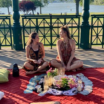 Two women sitting on a picnic blanket in a park.
