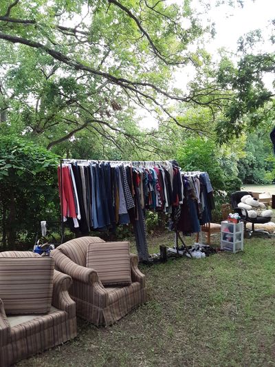 Outdoor clothes and furniture sale under a tree.